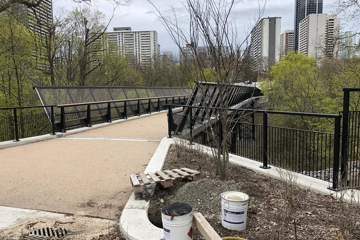 Bridge across ravine with trees and apartment buildings in background