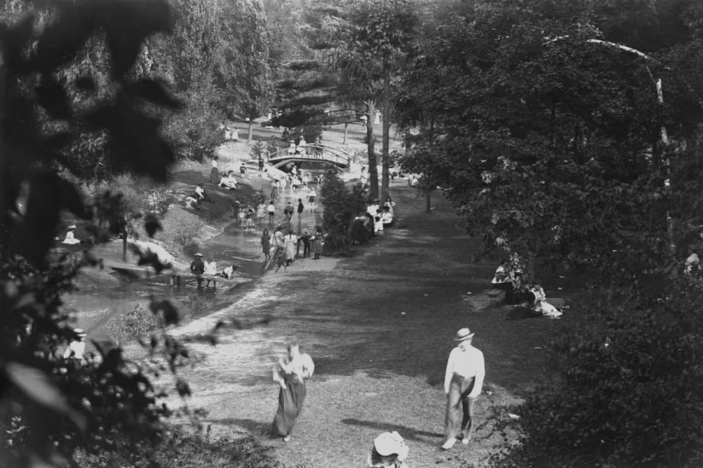 People enjoying a park with stream and woods in late 1800s.