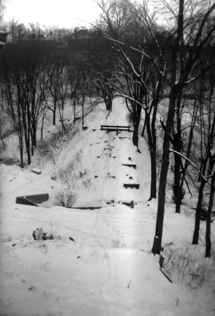 A snow-covered wooded landscape with a narrow path winding between bare trees.