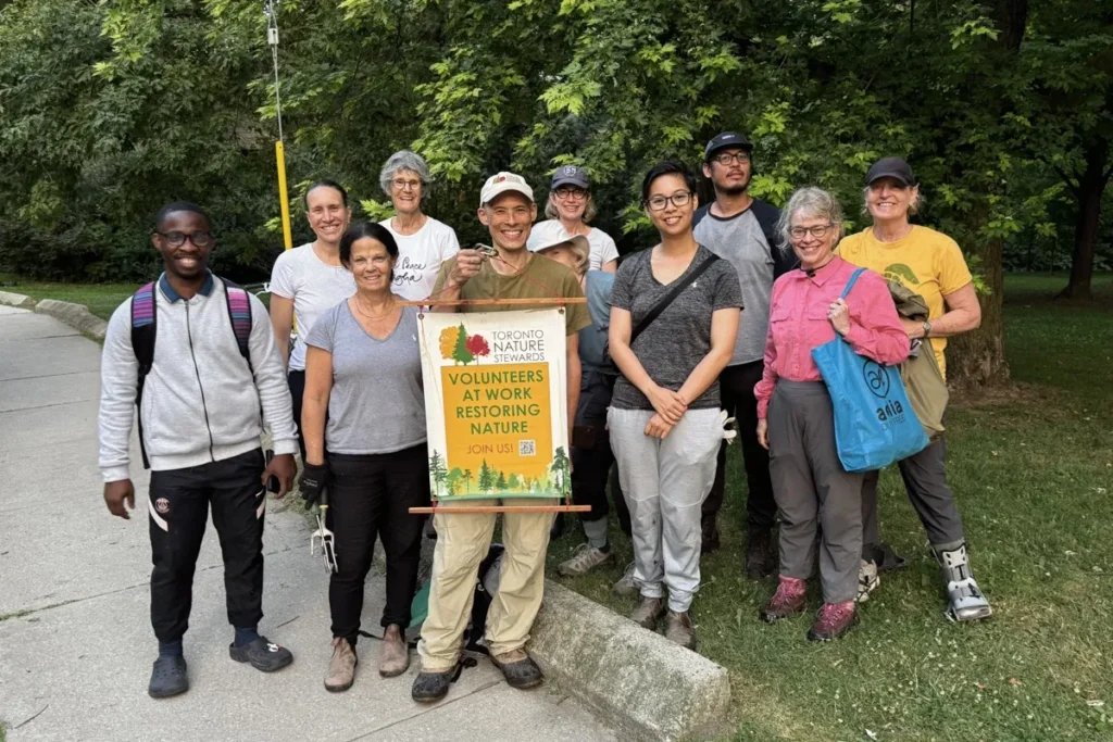 A group of hikers pose beside a trail sign reading &ldquo;Nature Center&rdquo; in a wooded park.