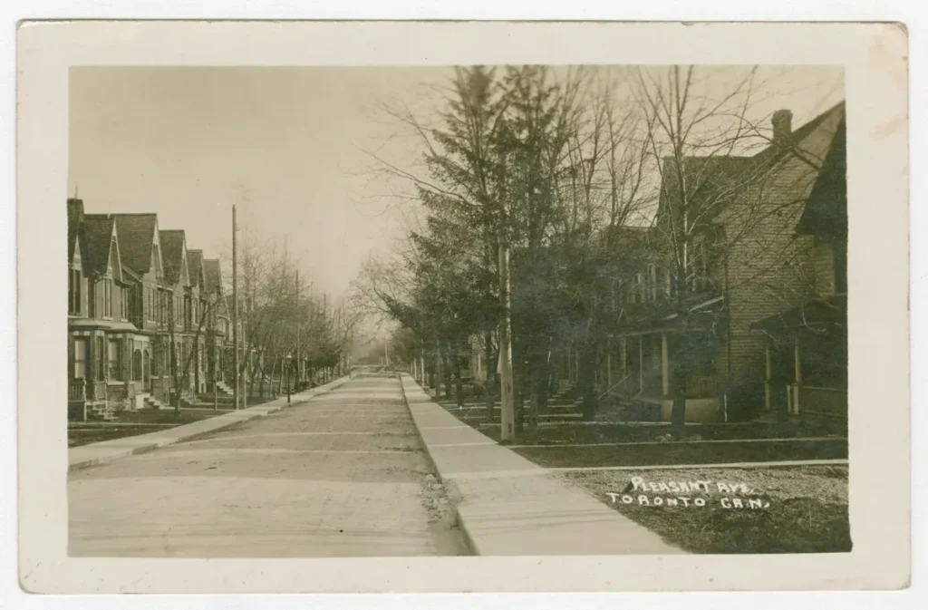 A vintage photograph of a quiet, tree-lined street with houses and a sidewalk.