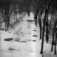 A snow-covered wooded landscape with a narrow path winding between bare trees.