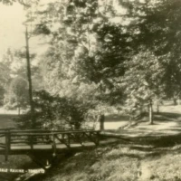 Sepia photograph of a wooded park with a rustic fence and a small caption reading “Rosebud Fishing Tr…”