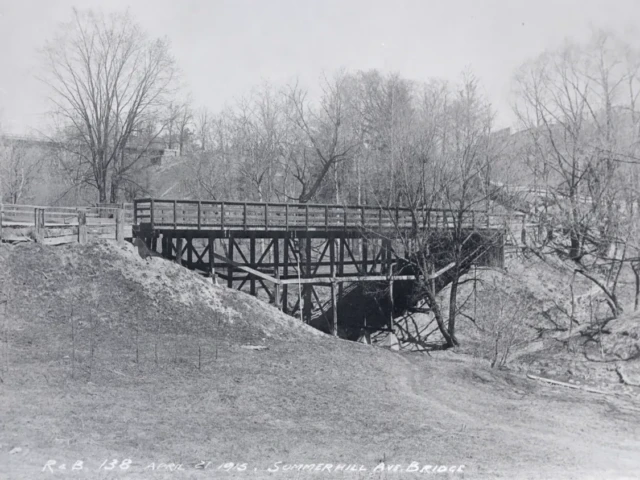 A wooden bridge crosses a snowy ravine among bare trees.