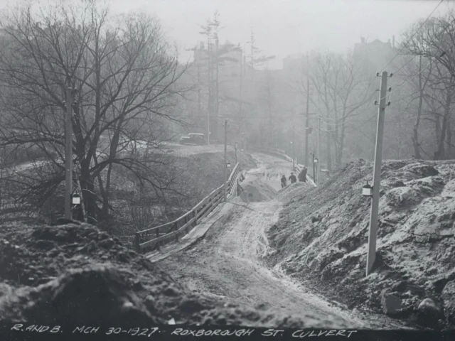A snowy rural road winds between bare trees and utility poles, with several people walking in the distance and a handwritten caption along the bottom.