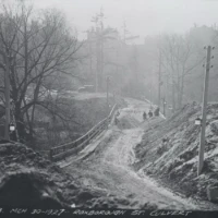 A snowy rural road winds between bare trees and utility poles, with several people walking in the distance and a handwritten caption along the bottom.