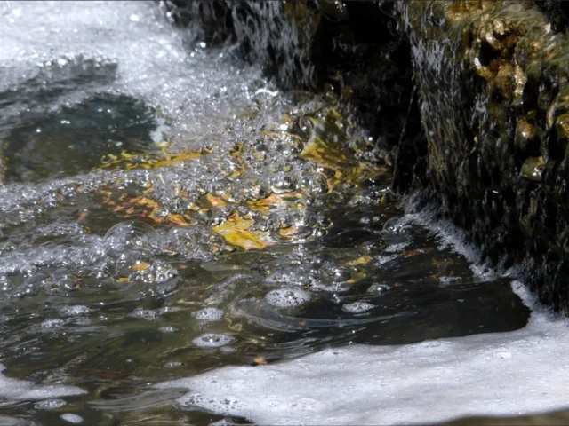 Water rushes over dark rocks into a foamy pool.
