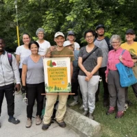 A group of hikers pose beside a trail sign reading “Nature Center” in a wooded park.