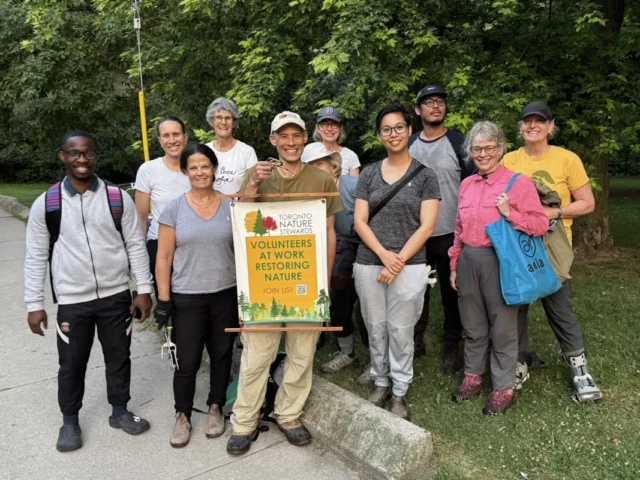 A group of hikers pose beside a trail sign reading “Nature Center” in a wooded park.