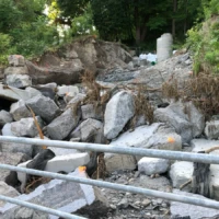 A rocky stream channel with a small trickle of water, metal railings, and dense trees and shrubs.