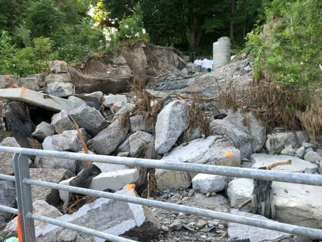 A rocky stream channel with a small trickle of water, metal railings, and dense trees and shrubs.