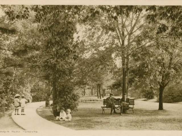 Sepia photograph of a horse-drawn carriage beneath trees in a park, with people walking along a path.