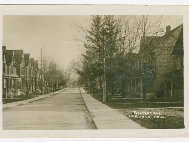 A vintage photograph of a quiet, tree-lined street with houses and a sidewalk.