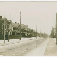 A snowy street lined with houses, utility poles, and bare trees.