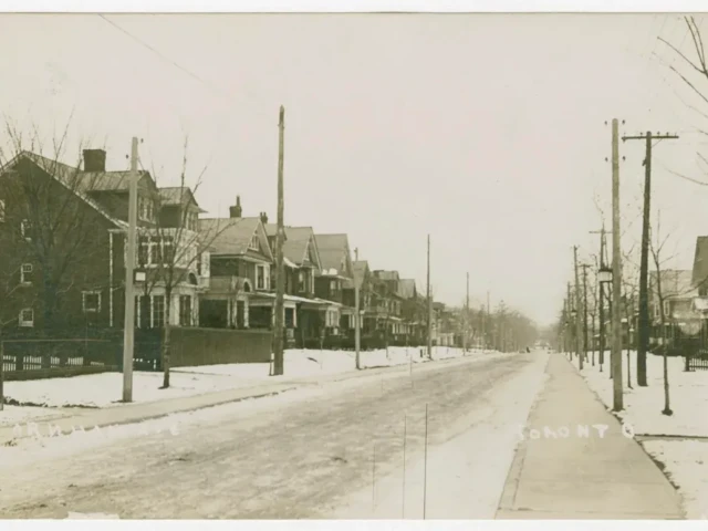 A snowy street lined with houses, utility poles, and bare trees.