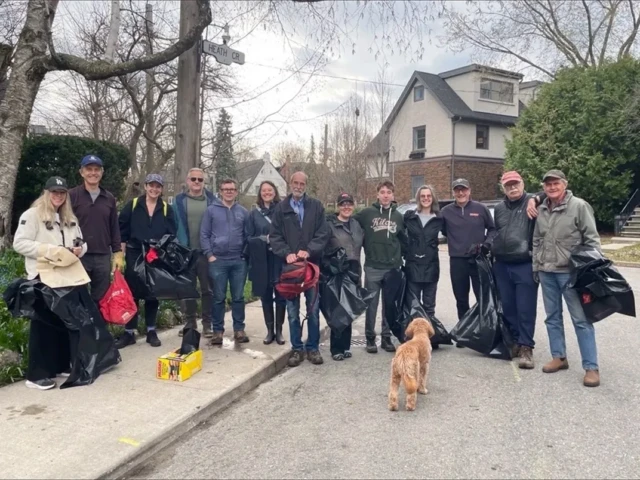 A group of people poses with a dog on a suburban street beside a pile of black bags.